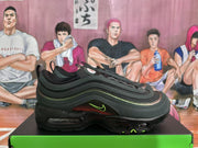 Side view of a black sneaker showing layered curved panels, green accent detailing, a small side logo, and visible sole windows.