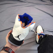 Rear view of the white high-top sneaker showing the Jumpman logo, blue padded collar, and orange patterned lining.