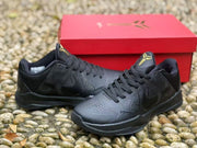 Pair of black Kobe 5 sneakers photographed on a pebble surface in front of a red shoe box.