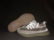 Cream-white Yeezy 350 V2-style kids sneakers shown under flash, highlighting the reflective-looking upper and translucent sole.