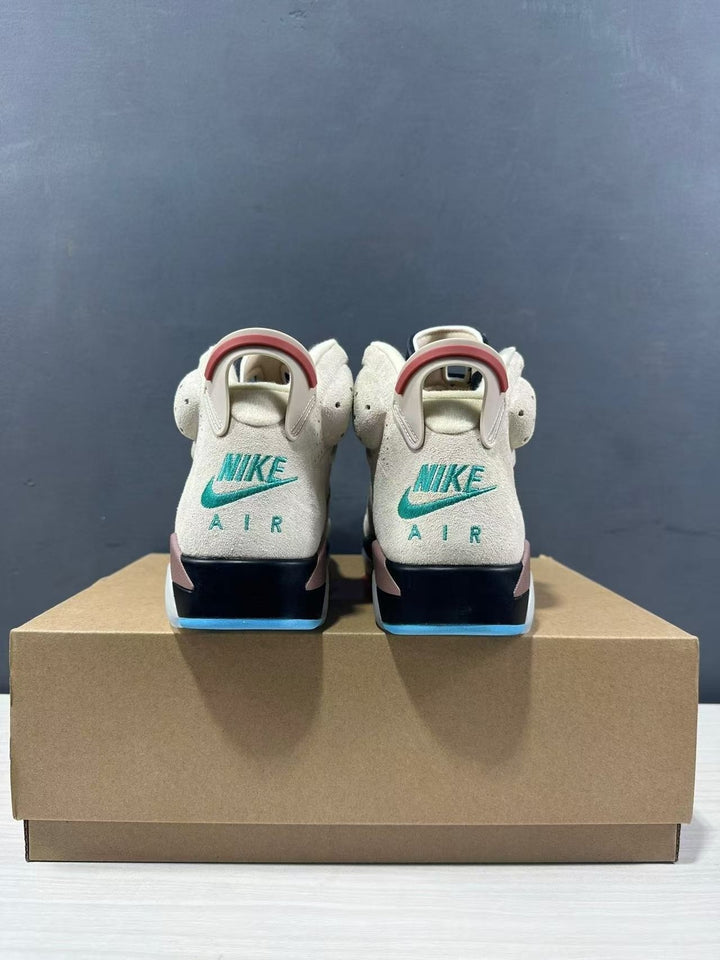 Rear view of light brown and cream high-top sneakers showing Jordan branding, padded collars, black midsoles, and blue outsole accents on a shoebox.