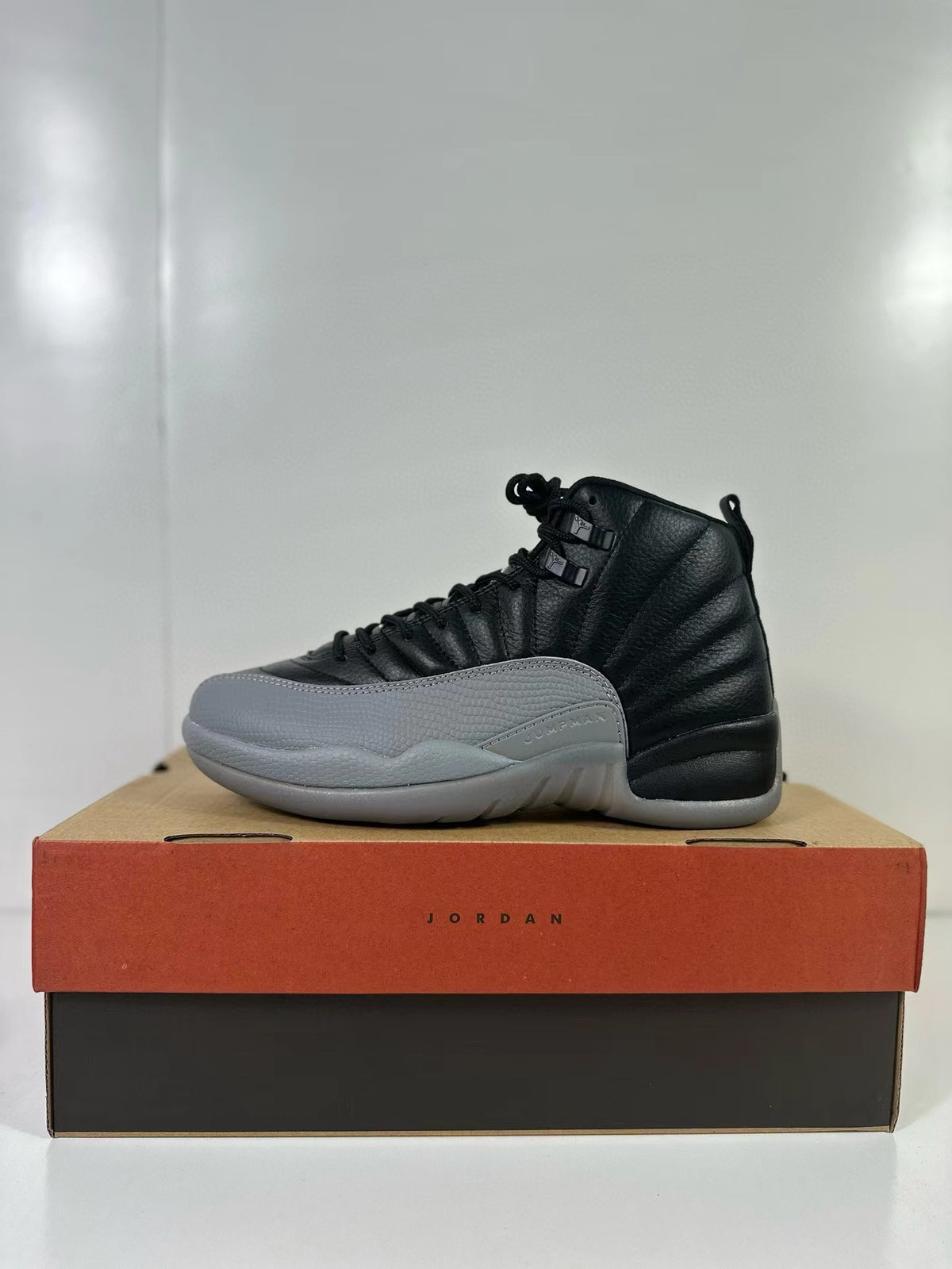 Side view of a black and grey Air Jordan 12 high-top sneaker on a shoebox