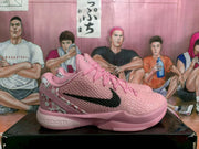 Side view of pink basketball sneakers with textured uppers, black side swooshes and floral heel panels on a black box.
