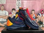 Angled view of the pair showing navy uppers, red laces, yellow-orange heel accents, perforated panels, and contrasting side graphics.