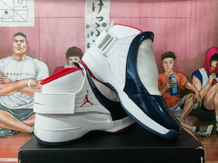 Pair of white and dark blue high-top basketball sneakers displayed on a black box, with red collar and outsole accents.