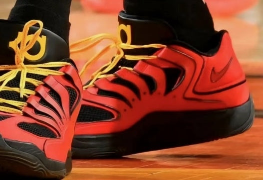 A pair of red and black high-top sneakers with yellow laces, layered panels, mesh sections, and a textured outsole.