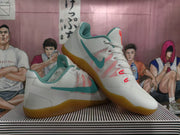 Angled view of white Nike Kobe basketball shoes with teal side detailing and gum-colored outsoles