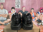 Rear view of a pair of black Nike sneakers showing pull tabs, padded collars, glossy heel panels, and textured uppers.