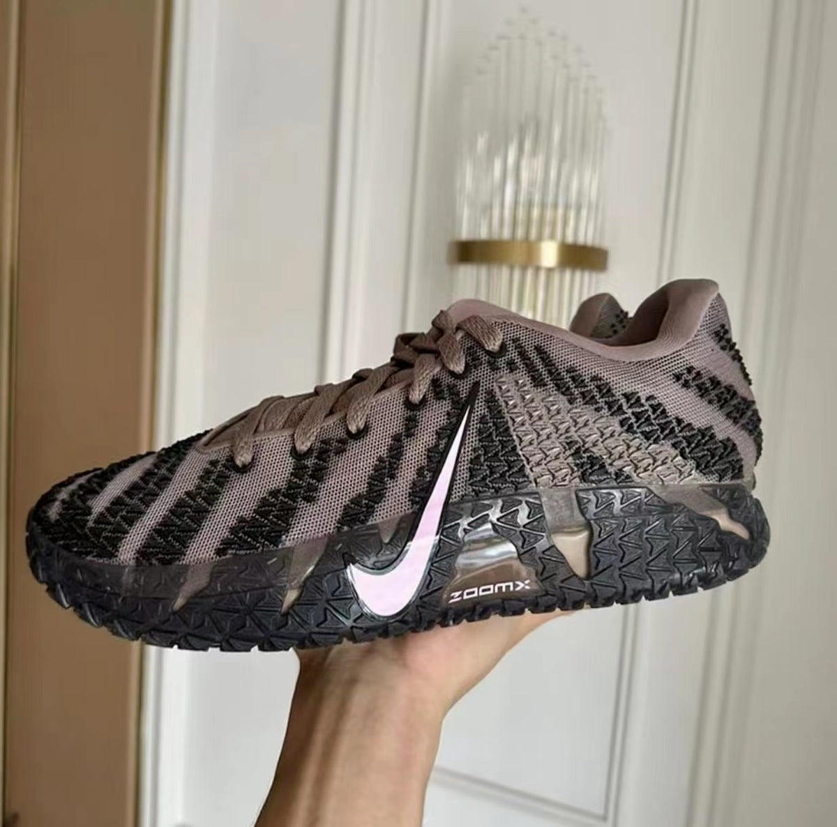 Side view of black and gray Nike sneakers with a pink Swoosh, brown laces, patterned upper, and rugged outsole.