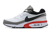 Side profile of a white Nike Air Max sneaker with grey trim, black Swoosh, and red heel detail.