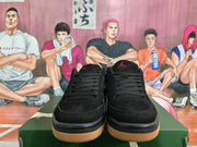 Front view of black low-top Jordan sneakers showing black laces, red tongue branding, and textured gum-colored outsoles.
