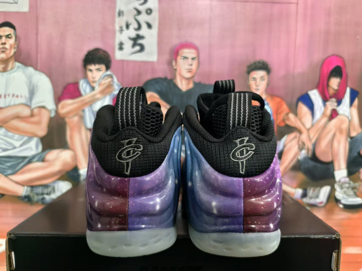 Rear view of black and purple-blue galaxy-patterned sneakers with translucent outsoles, displayed against an illustrated basketball-themed backdrop.