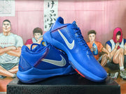 Blue Nike Kobe basketball shoes shown from the side with silver Swooshes and red stitching