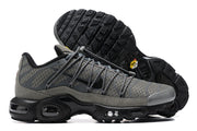 Side view of grey Nike Air Max Plus sneakers showing the patterned upper and black sole.