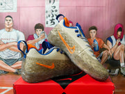 Side view of beige Nike sneakers with an orange Swoosh, blue details, and speckled outsole.
