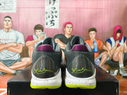 Rear view of Nike basketball shoes with charcoal heels, purple collar accents, speckled white midsoles, and yellow-green outsoles.