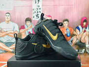 Pair of black basketball shoes with gold side detailing and circular Kobe logo accessories.