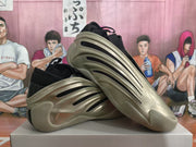 Angled view highlighting the metallic gold upper, black side cutouts, and sculpted outsole.