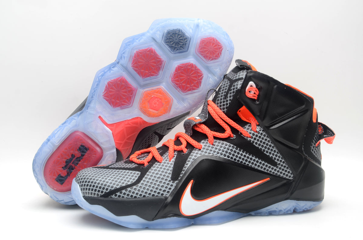 Black and grey Nike high-top basketball sneakers with orange laces, bright accents and a translucent outsole shown from the side.