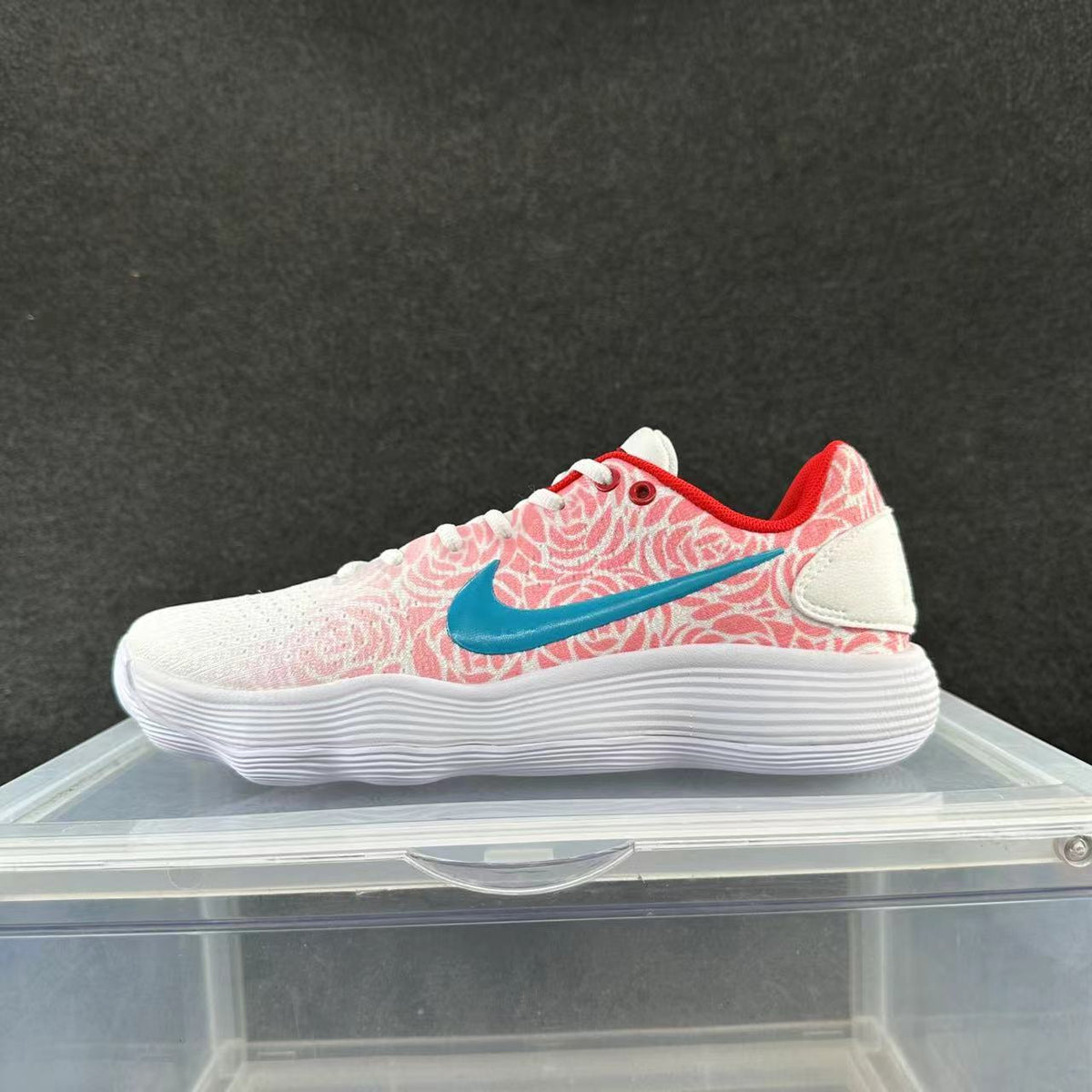 Low-top sneaker with a white toe and sole, pink-red patterned panels, blue Swoosh, and red collar trim