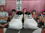 Front view of white basketball shoes with black tongues, white laces, and gold details.