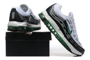 White, black, and green Nike sneakers shown from the heel and side on a black shoe box.