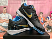 Angled view highlighting the black upper, gold and blue Swoosh, perforated forefoot, and translucent outsole.