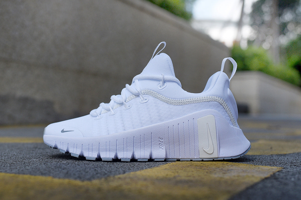 Side view of a white Nike low-cut training shoe with lace-up closure, pull tabs, and a sculpted outsole.