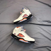 Pair of white high-top sneakers arranged on gray fabric, displaying the side panels, orange midsole accents, and translucent outsole.