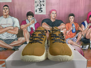 Front view of gold-brown low-top sneakers with black patterned laces and contrasting off-white soles.