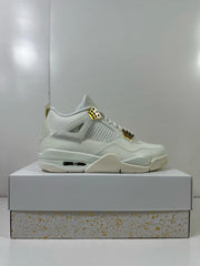 Side profile of white Jordan 4 sneakers with gold-tone lace hardware displayed on a shoebox.
