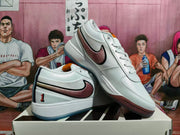 Angled view of white low-top sneakers with burgundy side accents, striped heel details, and contrasting soles.
