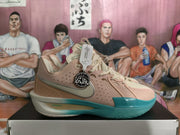 Side view of a pink Nike basketball sneaker showing perforations, silver Swoosh branding, teal outsole, and circular side charm.