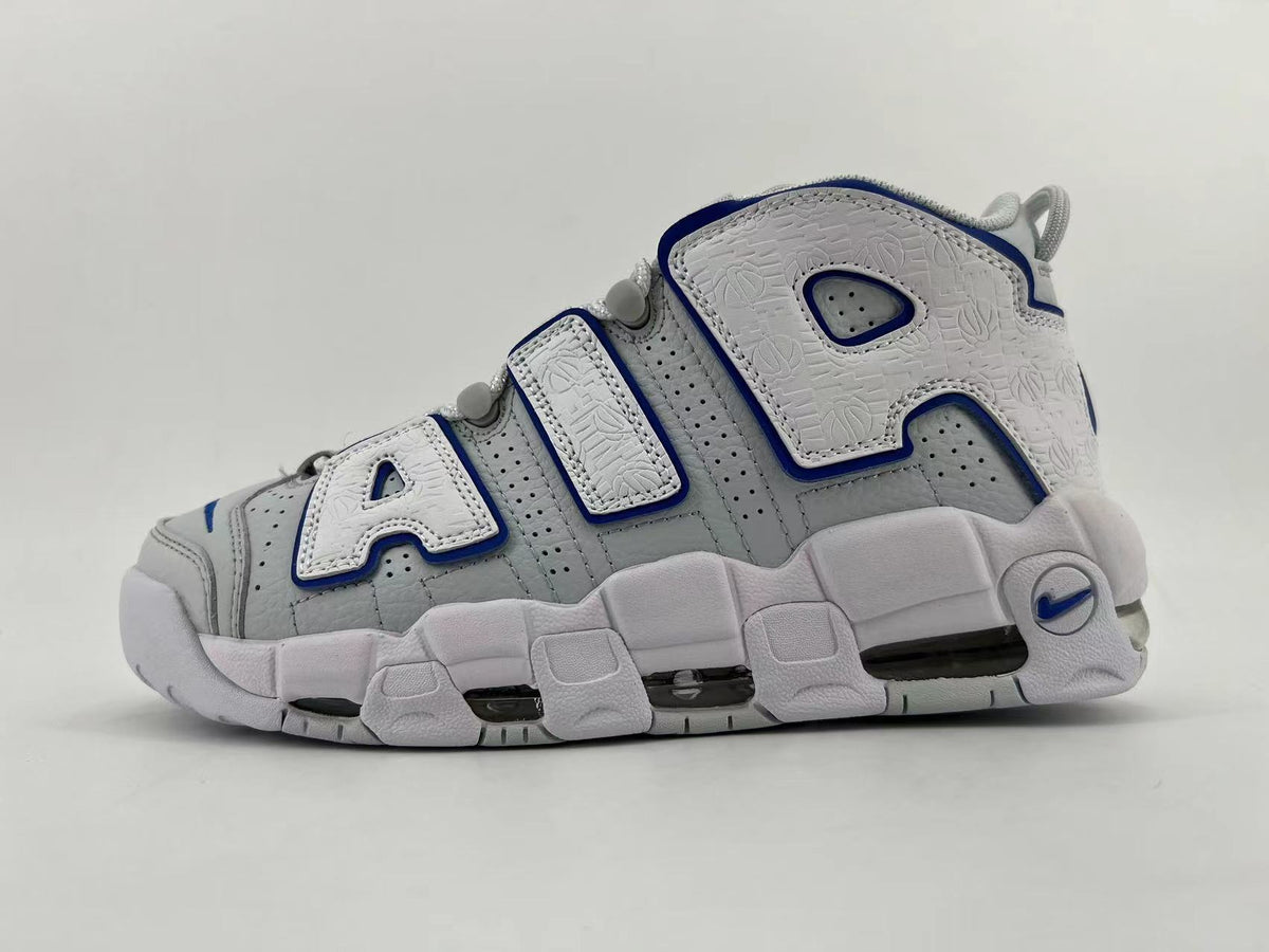 Side view of white and light gray Nike Air More Uptempo sneakers with oversized white AIR lettering outlined in blue and a chunky sole.