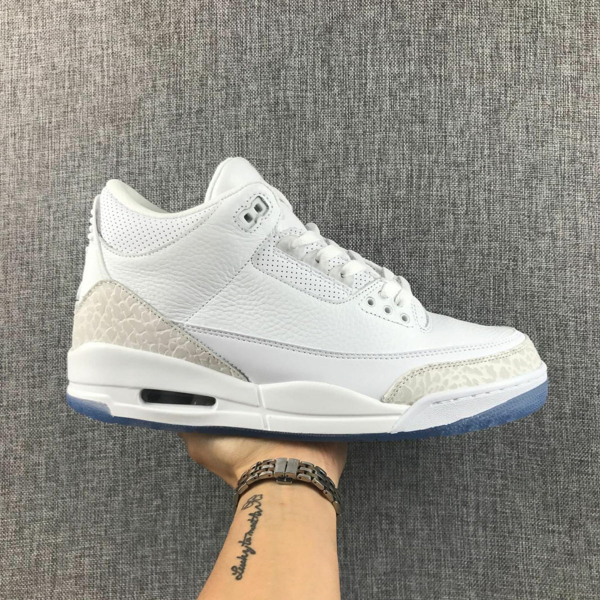 Side profile of a white Jordan 3 sneaker with light gray textured overlays and an icy blue outsole.