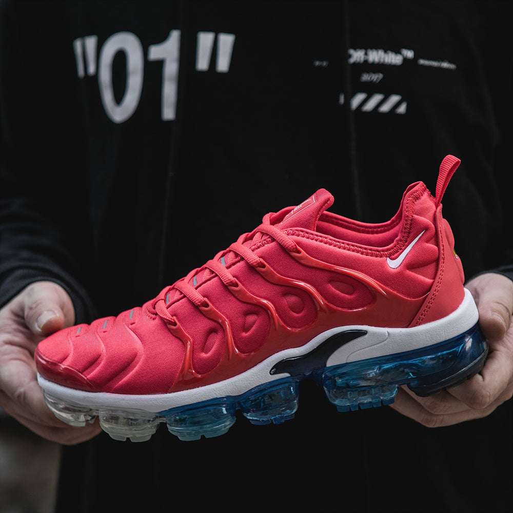 Close-up of a red Nike Air VaporMax Plus sneaker with white midsole and blue translucent cushioning pods.