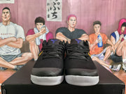 Front view of the black sneaker pair showing black laces, textured uppers, yellow side accents, and white toe outsoles.