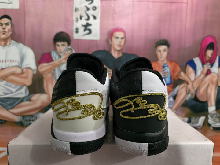 Rear view of black-and-white basketball sneakers with gold script-style heel detailing and contrasting outsoles.