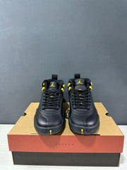 Front view of a pair of black and yellow Jordan Air Jordan 12 Retro sneakers with black laces and yellow tongue branding.