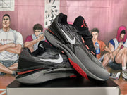 Angled view of black Nike sneakers with white swooshes, gray layered midsoles, and red outsole accents.