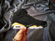 Side profile of a black and gold Jordan Air Jordan 6 sneaker held against a gray fabric background.