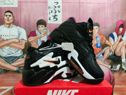 Angled view of black Nike sneakers showing white side panels, orange accents, and layered soles.
