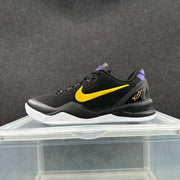 Side profile of a black low-top basketball sneaker with a gold Swoosh, purple heel accent, and white outsole.