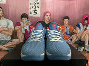 Front view of Nike Zoom basketball sneakers with textured blue uppers, white laces, black tongue logos, and orange accents.