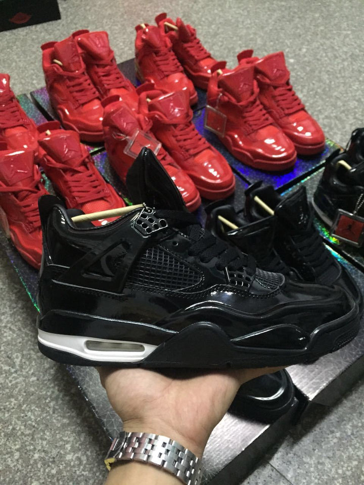 Black and red high-top sneakers displayed on patterned boxes; a glossy black Jordan 4-style shoe is held in the foreground.