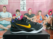 Side profile of a black Nike basketball sneaker with a gold Swoosh, purple heel detail and white outsole.