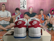 Rear view of white Nike sneakers with red heel panels and blue outsole accents on a shoebox.