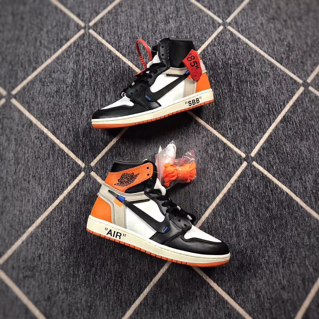 Pair of black, white, and orange Air Jordan 1 high-top sneakers displayed from the side with alternate orange laces.
