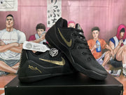Angled view showing the black lace-up Nike basketball sneakers, gold Swoosh detailing, and padded collar.