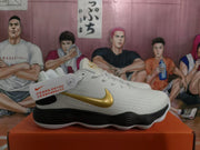 Side view of a white Nike basketball sneaker with a gold Swoosh, black heel section and black layered midsole.